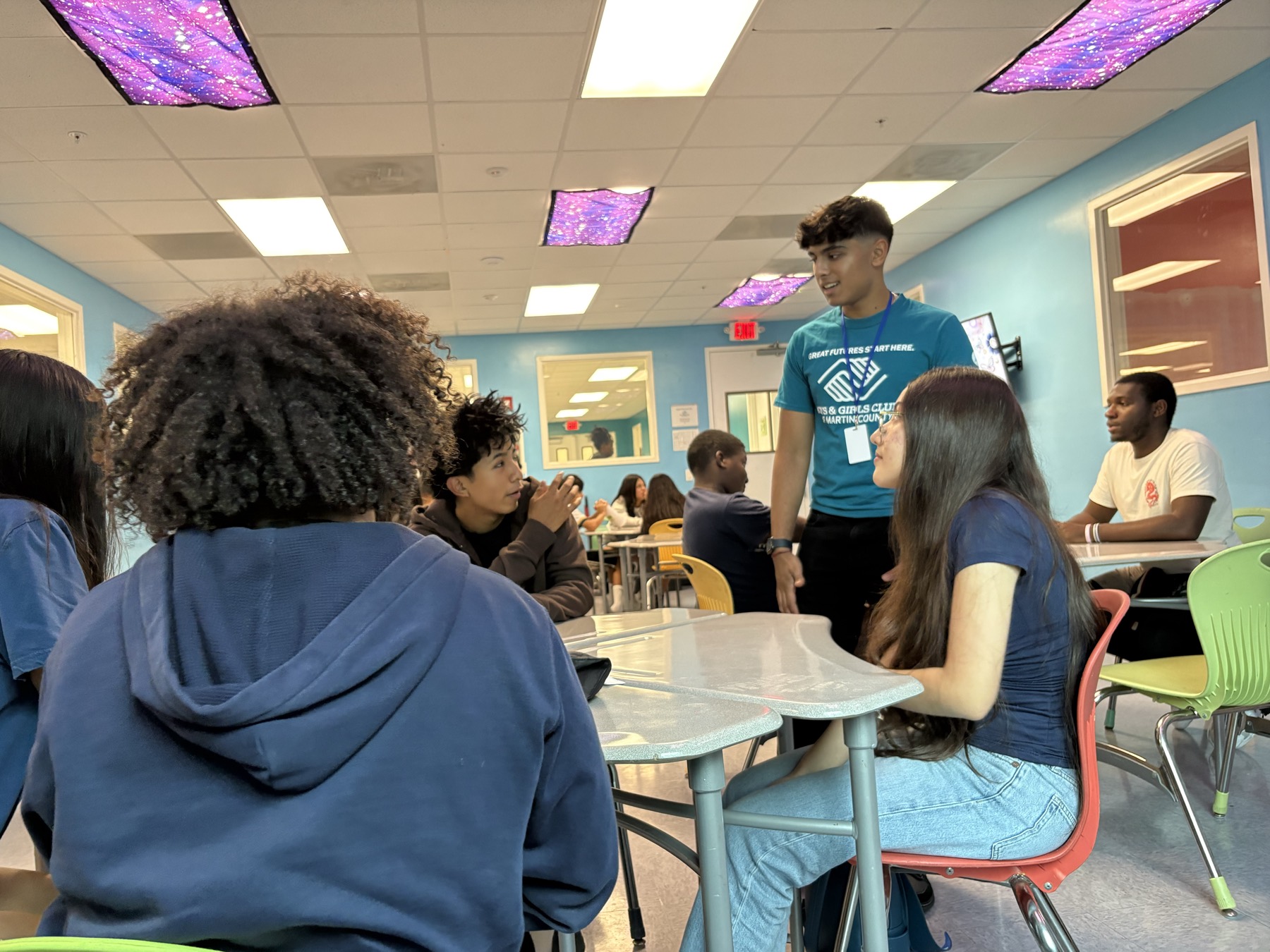 A Speak2Achieve volunteer talking with students seated around a table during a workshop