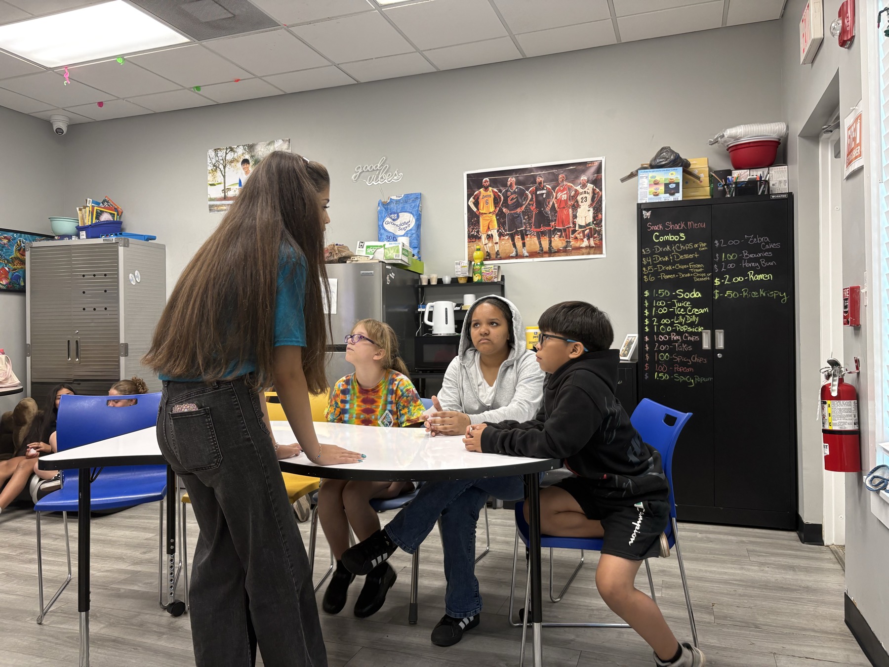 A volunteer standing at a table talking with three students seated together