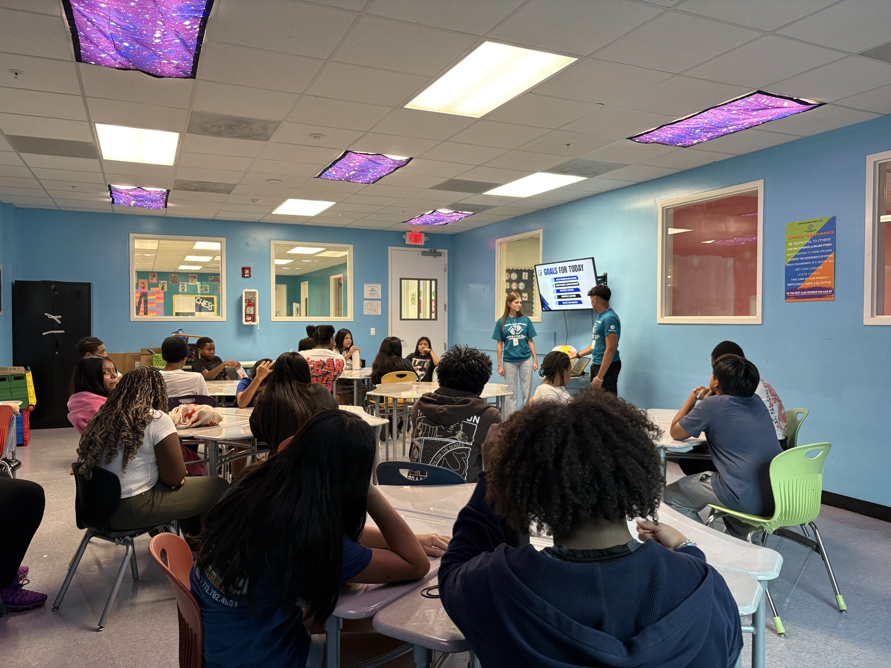Two Speak2Achieve volunteers presenting to a full classroom of seated students